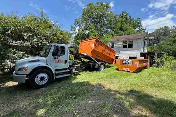 Big Orange truck delivering an orange roll-off dumpster beside a home
